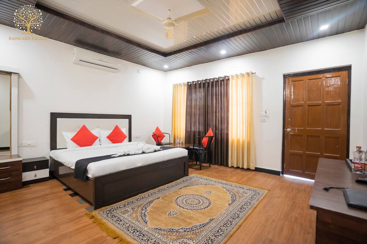 A hotel room with a bed, a desk, a chair, a rug, and a wooden door.