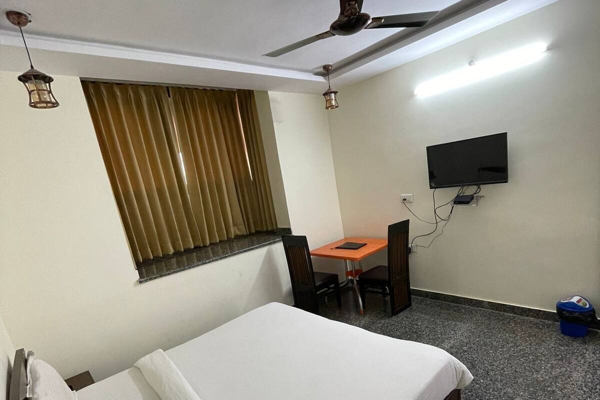 A hotel room with a bed, a desk, a chair, a television, and a ceiling fan.