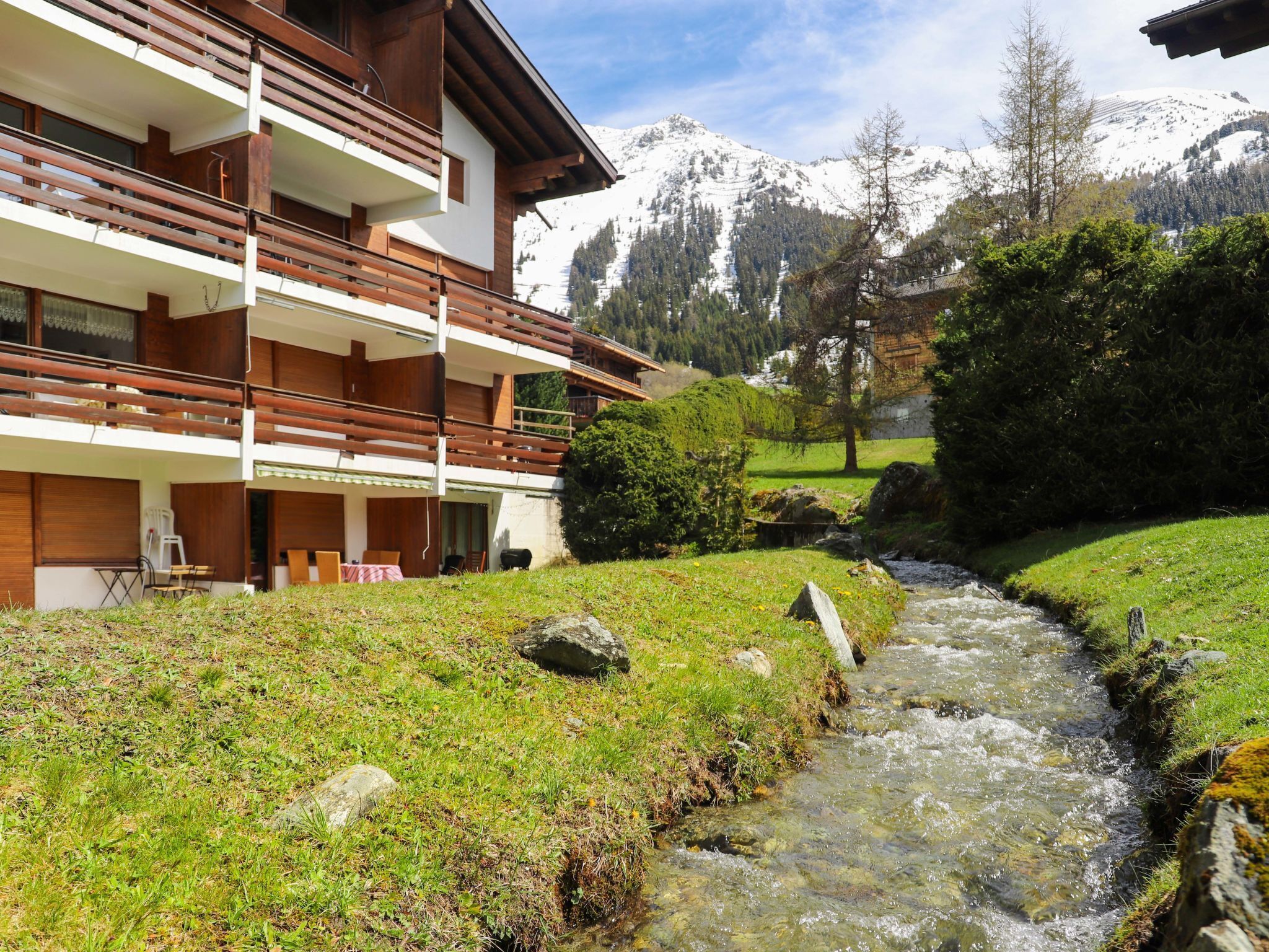 Un edificio moderno con varios balcones que dan a un arroyo y un paisaje montañoso.