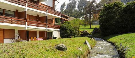 Un edificio moderno con varios balcones que dan a un arroyo y un paisaje montañoso.