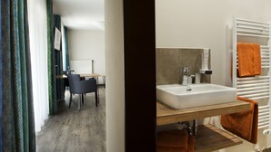 A modern bathroom with a white sink, wooden shelves, and a towel rack with an orange towel. - Hotel Zum Grünen Baum (Ellwangen)