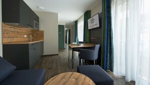 A modern hotel room with a kitchenette, a dining area, and a seating area with a wooden table. - Hotel Zum Grünen Baum (Ellwangen)
