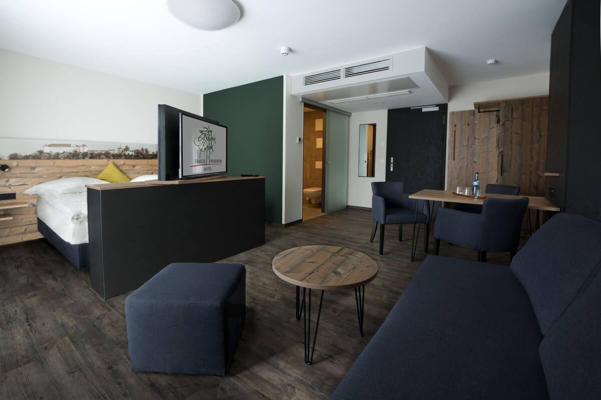 A modern hotel room with a bed, a desk, a sofa, and a small round table.