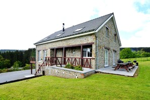 Een stenen huis met een overdekte veranda, een barbecueplek en uitzicht op het omliggende landschap.