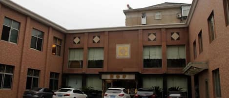 Un edificio con entrada central, varias ventanas y un estacionamiento con varios coches.