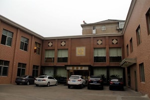Un edificio con entrada central, varias ventanas y un estacionamiento con varios coches.