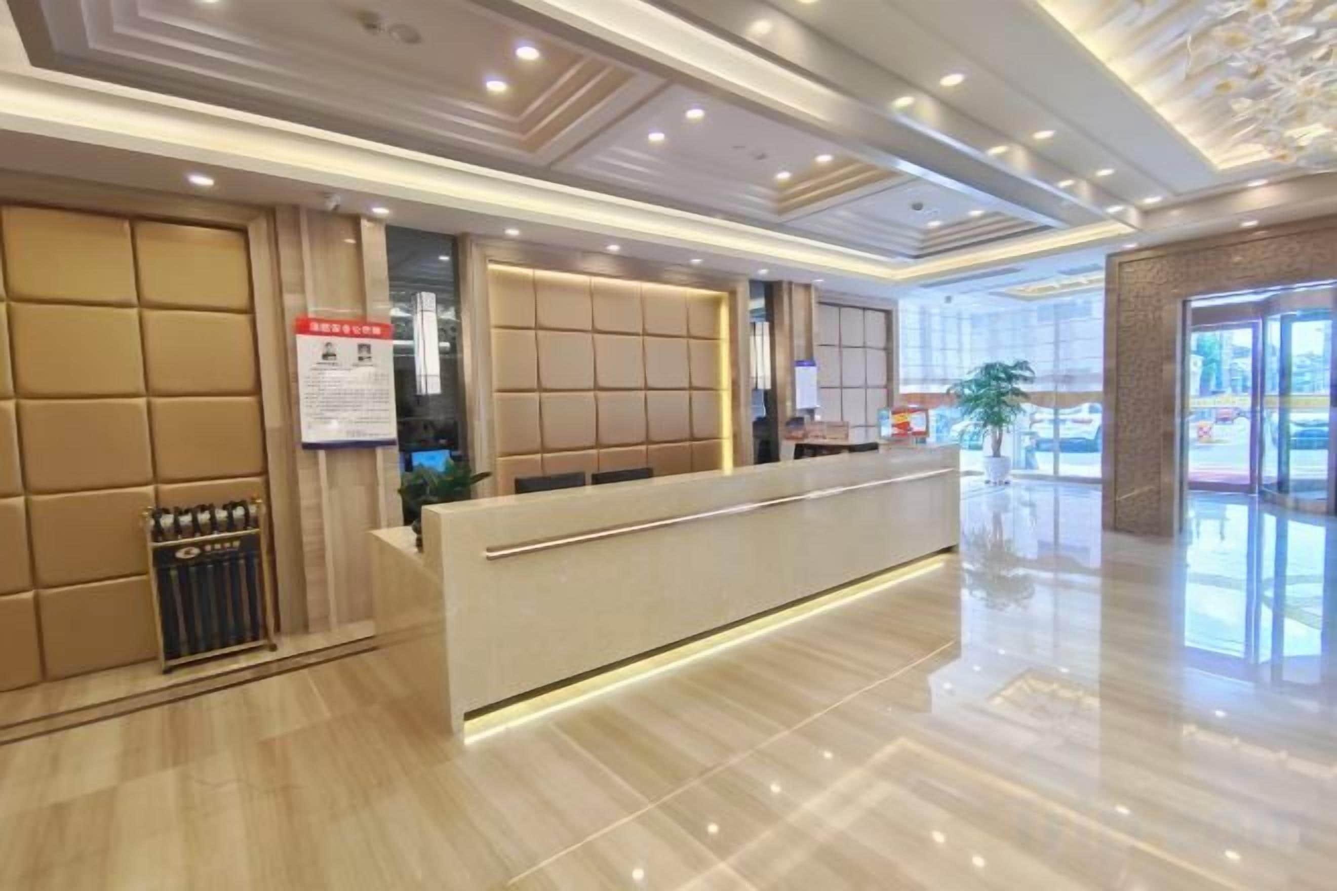 A hotel reception area with a modern design, including a reception desk, a seating area, and a large window offering a view of the outside.