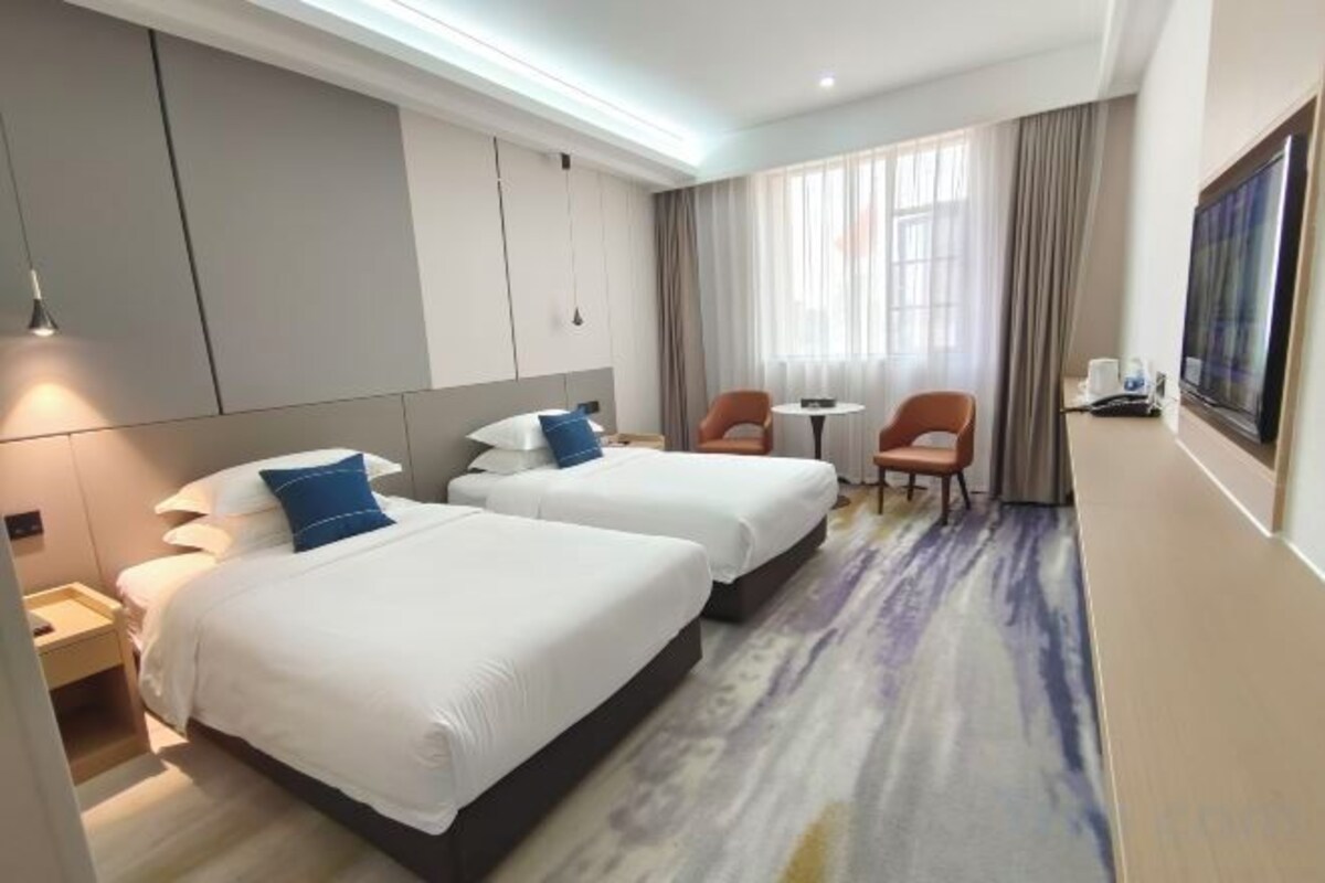 A hotel room with two beds, a desk, a chair, a TV, and a window with curtains.