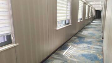 A hallway with a patterned carpet, wooden walls, and windows with blinds.
