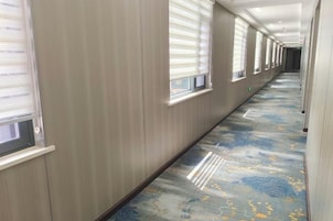 Un pasillo con alfombra estampada, paredes de madera y ventanas con persianas.