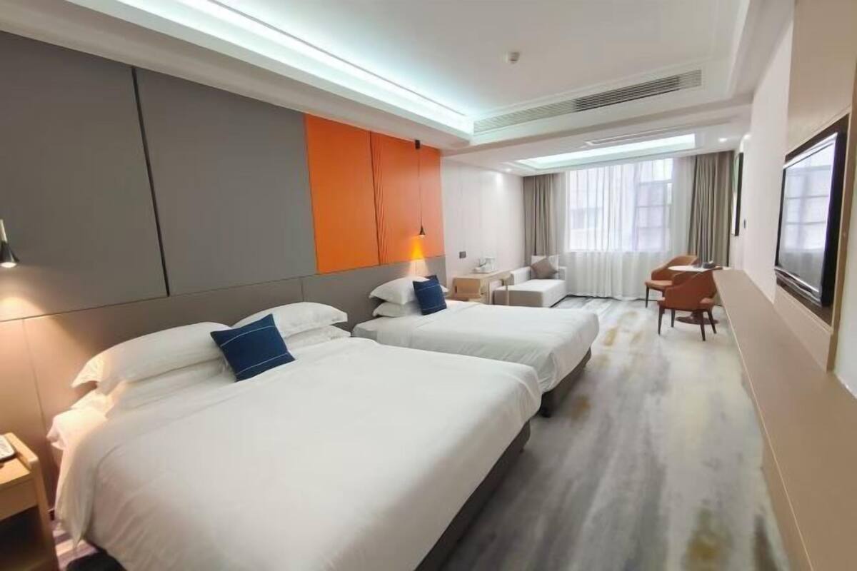 A hotel room with two beds, a desk, a chair, and a TV.