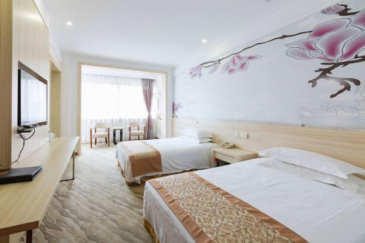 A hotel room with two beds, a desk, and a large floral mural on the wall.