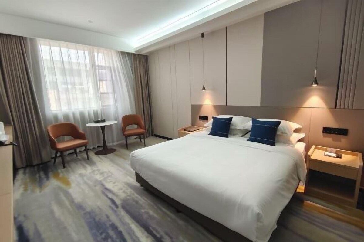 A hotel room with a large bed, two chairs, a small table, and a nightstand with a lamp.