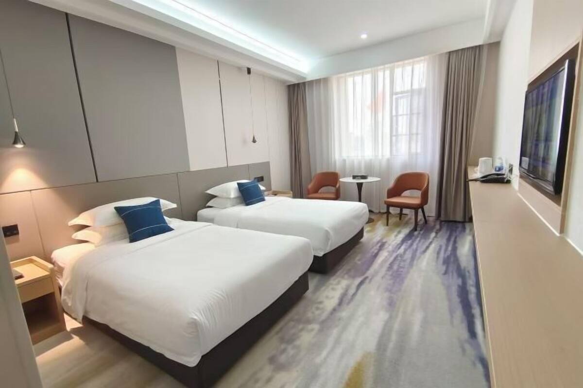 A hotel room with two beds, a small table, a chair, and a TV.