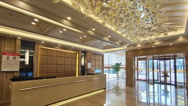 Zona de recepción de hotel con diseño moderno, que incluye un mostrador de recepción, área de estar y un techo decorativo.