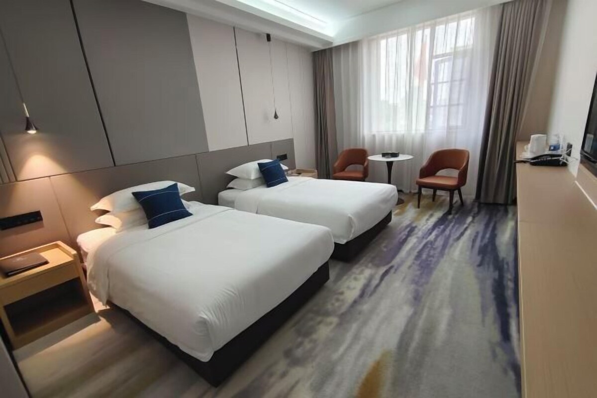 A hotel room with two beds, a desk, a chair, and a TV.