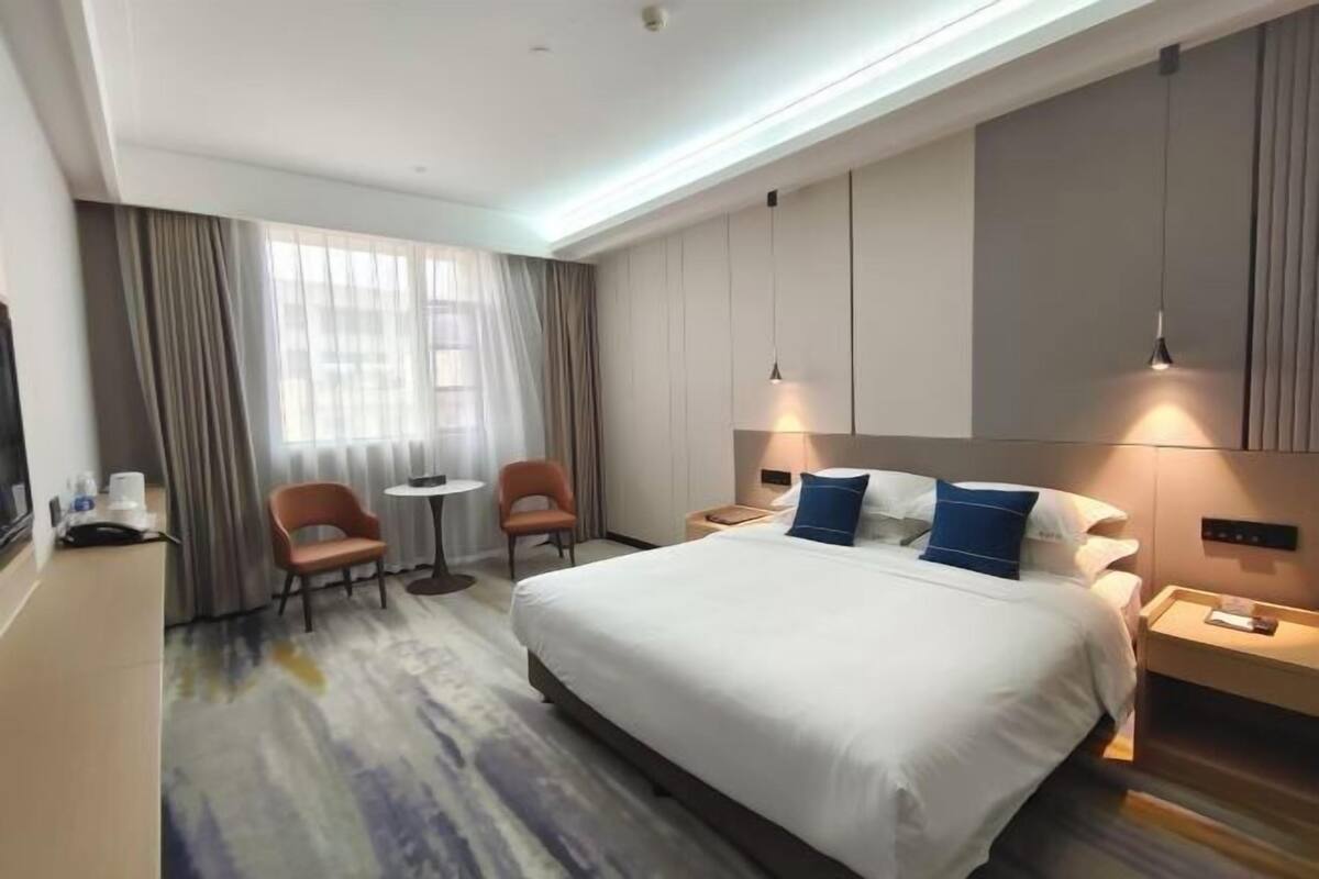 A hotel room with a large bed, two chairs, a small table, and a TV.