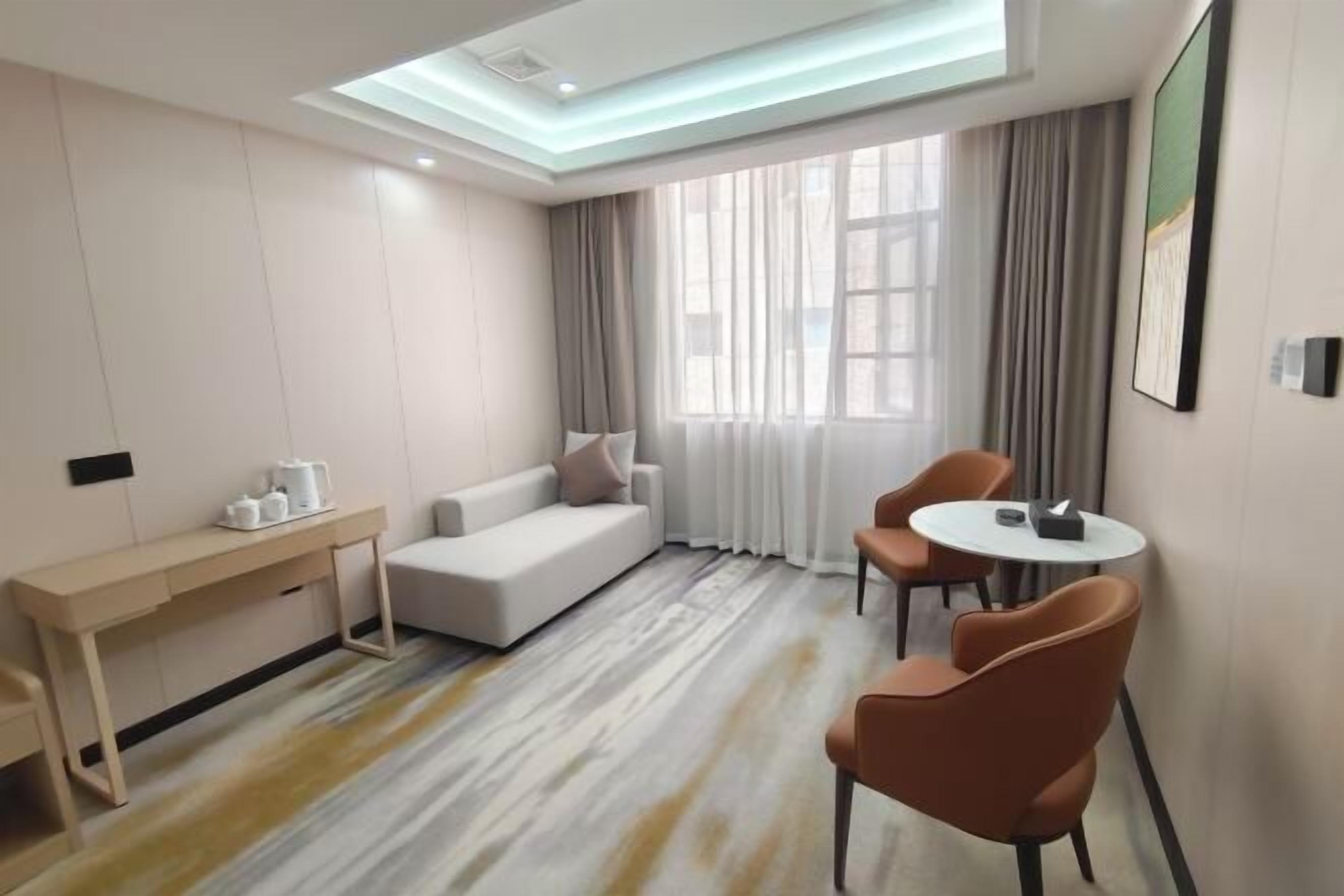A modern hotel room with a sofa, two chairs, a small table, and a desk.