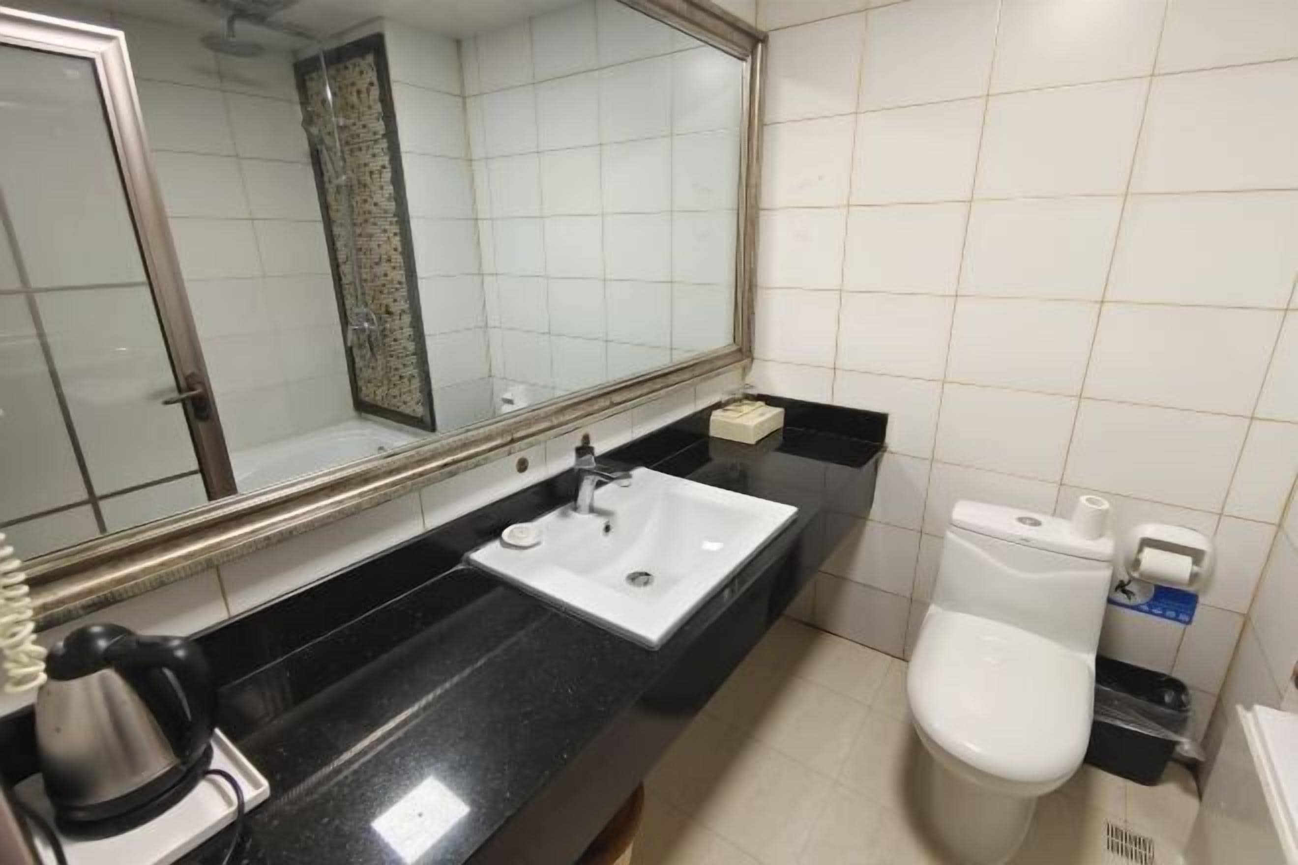 A bathroom with a black countertop, a white sink, a mirror, a toilet, and a trash bin.