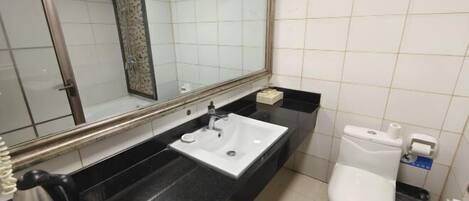 A bathroom with a black countertop, a white sink, a mirror, a toilet, and a trash bin.
