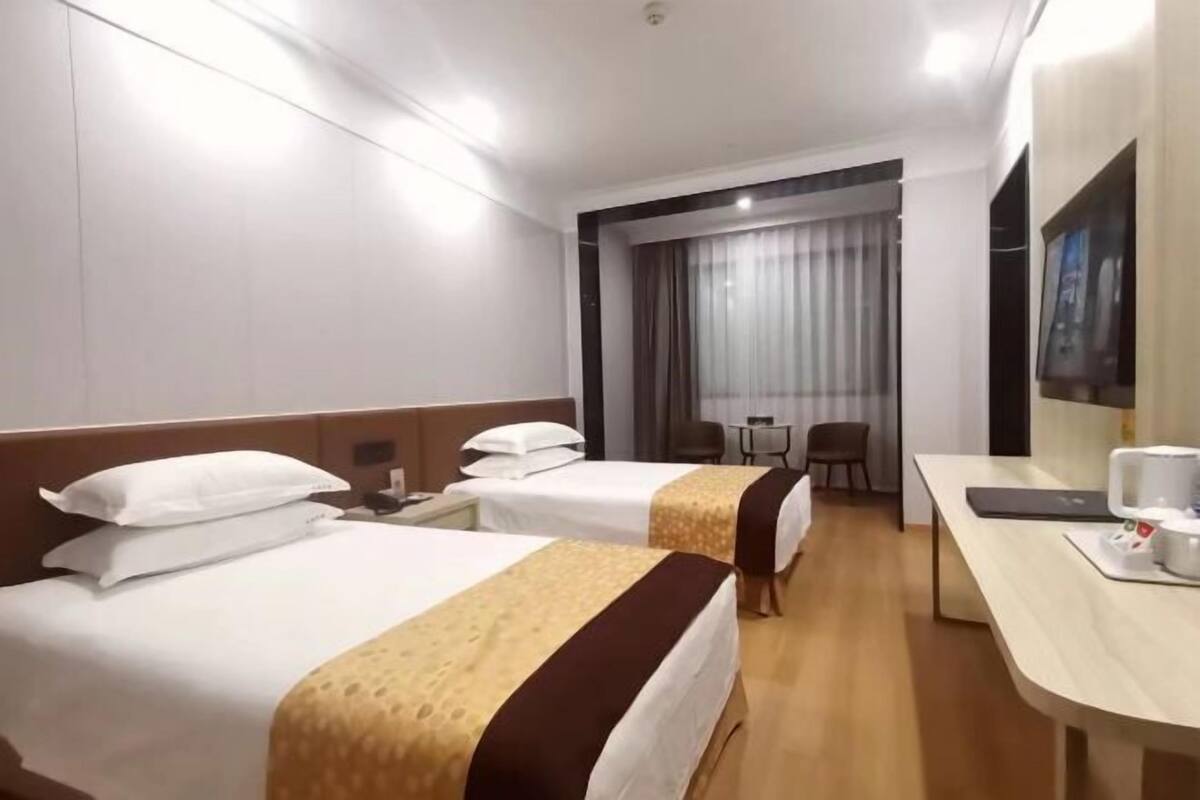 A hotel room with two beds, a desk, a chair, a small table, and a window with curtains.