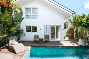 A white house with a wooden deck, a pool, and outdoor furniture. - Sun & Moon Villa (Canggu)