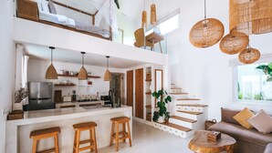 A modern kitchen with a central island, wooden stools, and a dining area with a round wooden table. - Sun & Moon Villa (Canggu)