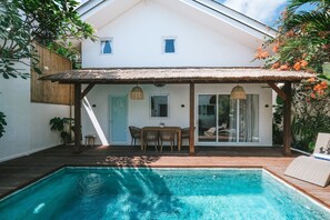A poolside area with a covered patio, a table with chairs, and a lounge chair. - Sun & Moon Villa (Canggu)