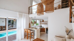 A modern, open-plan living space with a kitchen, dining area, and a view of a swimming pool. - Sun & Moon Villa (Canggu)