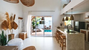 A modern kitchen with a large island, bar stools, and a sliding glass door leading to a pool area. - Sun & Moon Villa (Canggu)