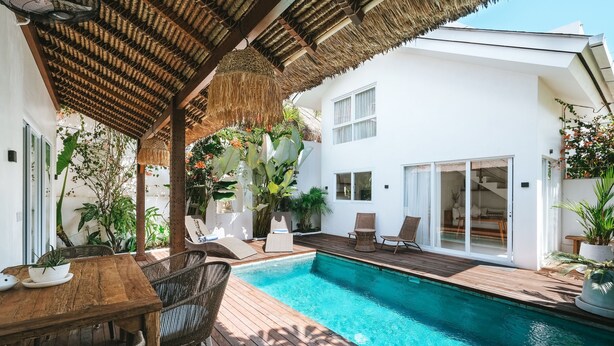 A pool area with a wooden deck, wicker furniture, and a thatched roof structure. - Sun & Moon Villa (Canggu)