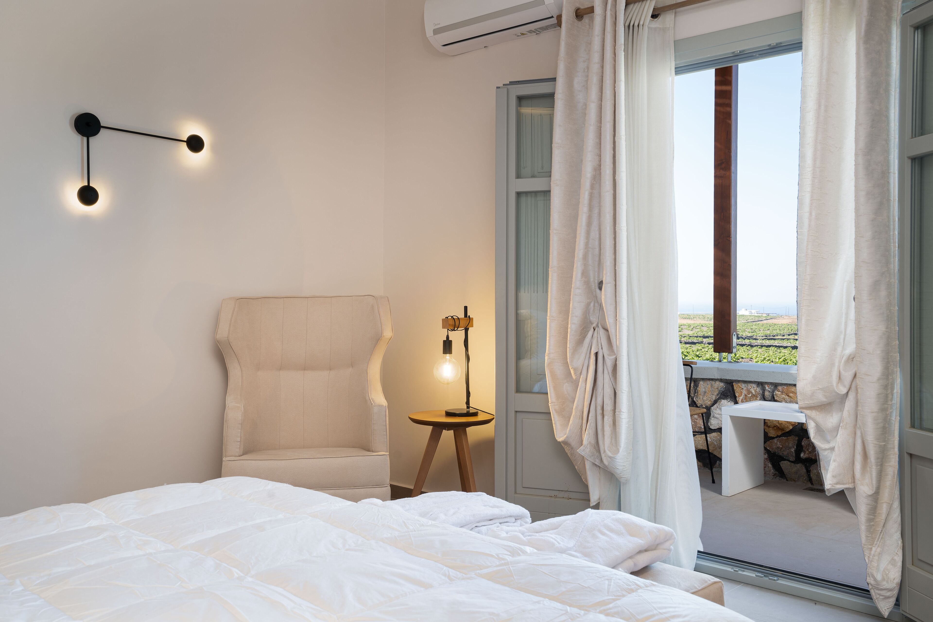 Une chambre à coucher comprenant un lit, une chaise, une table et donnant sur l’extérieur.