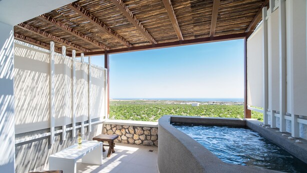 A terrace with a stone wall, a wooden bench, a small table, and a hot tub. - New Villa Katerina Collection (Santorini)