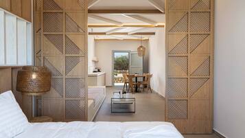 A modern bedroom with a large bed, a bedside lamp, and a view into a dining area with a table and chairs.