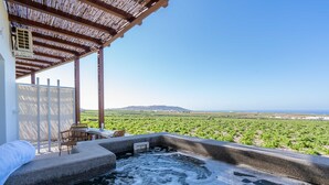 A hot tub with a view of a vineyard, a pergola, and a table with chairs. - New Villa Katerina Collection (Santorini)