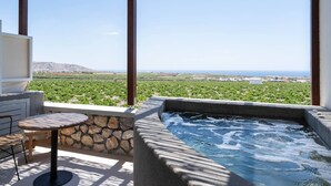 A rooftop terrace with a hot tub, stone walls, and a view of a vineyard and coastline. - New Villa Katerina Collection (Santorini)