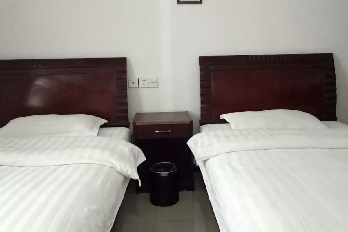 A hotel room with two single beds, a nightstand, a trash bin, and a wall socket.