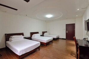A hotel room with three single beds, a wooden desk, a TV, and a door.