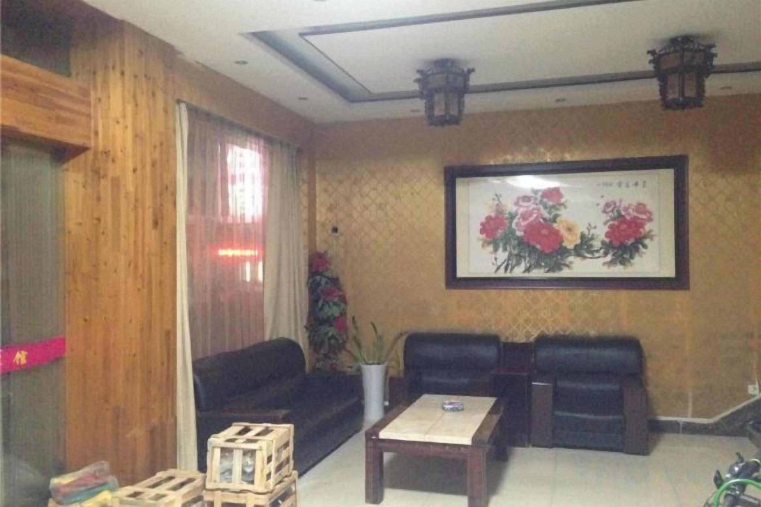 A room with a wooden wall, a black sofa, a coffee table, and a framed floral painting.