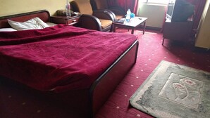A hotel room with a bed, a chair, a small table, a television, and a carpeted floor. - Hotel Al Bader (Mekhtar)