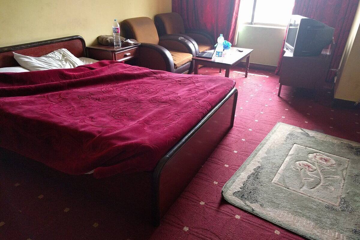 A hotel room with a bed, a chair, a small table, a television, and a carpeted floor.