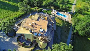 An aerial view of a large house with a swimming pool, a covered patio, and a circular driveway.