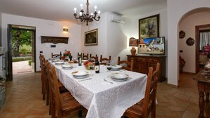 A dining room with a long table set for a meal, wooden chairs, a chandelier, and a painting on the wall.