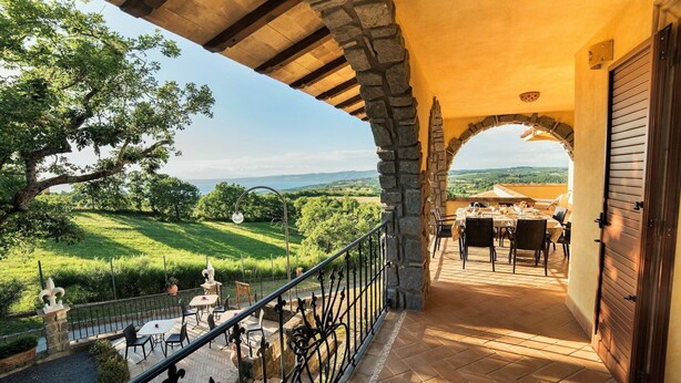 A balcony with a stone archway, outdoor seating, and a view of a green landscape.