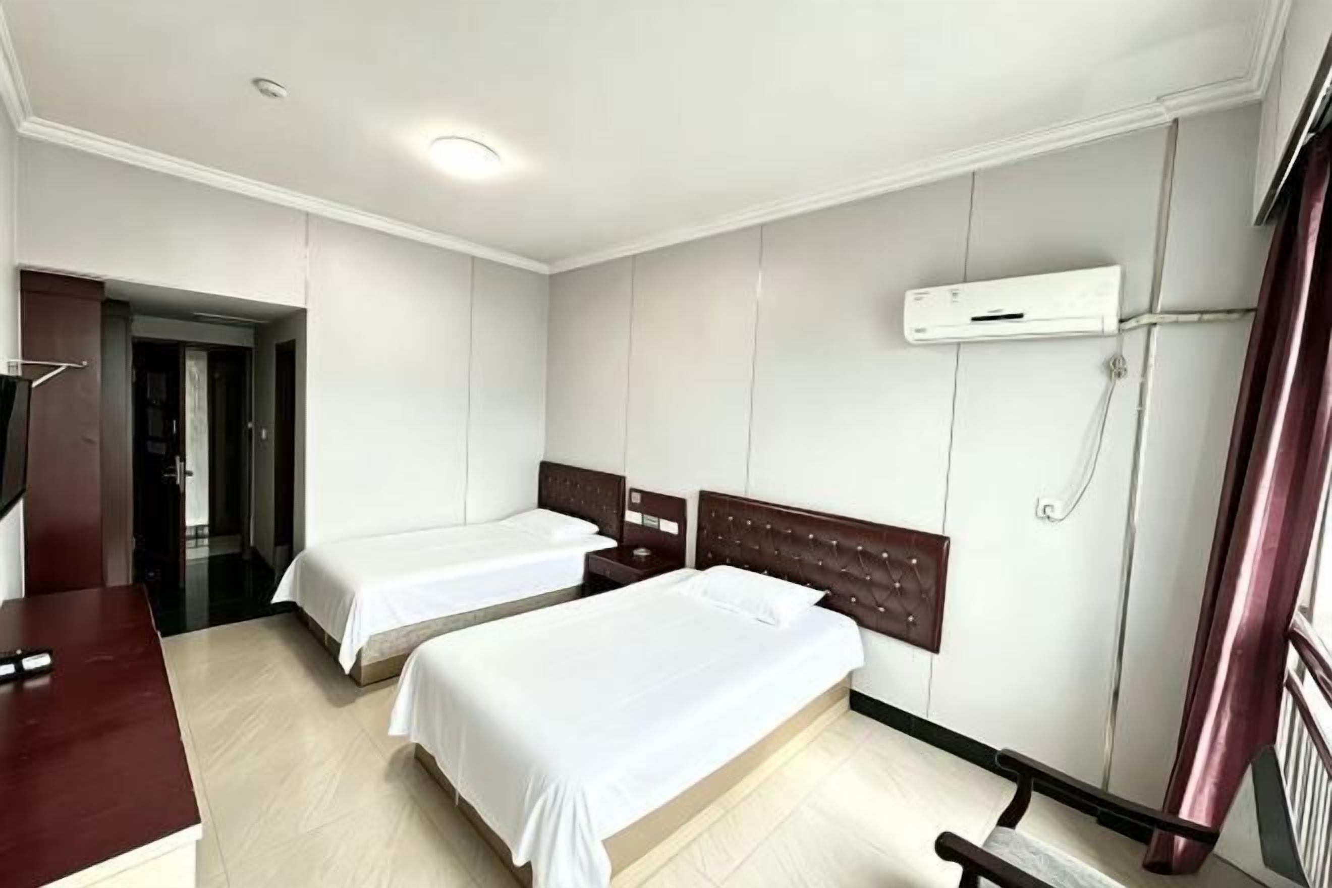A hotel room with two beds, a desk, and a TV.