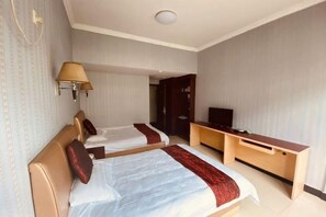 Habitación de hotel con dos camas, un escritorio, un televisor y una lámpara.