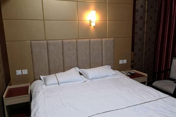 A hotel room with a large bed, a nightstand, a wall-mounted light, and a chair.