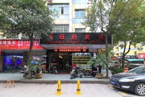 A hotel with a prominent sign, outdoor seating, and a parking area. - Chuang Wang Fu Hotel (Yiwu)