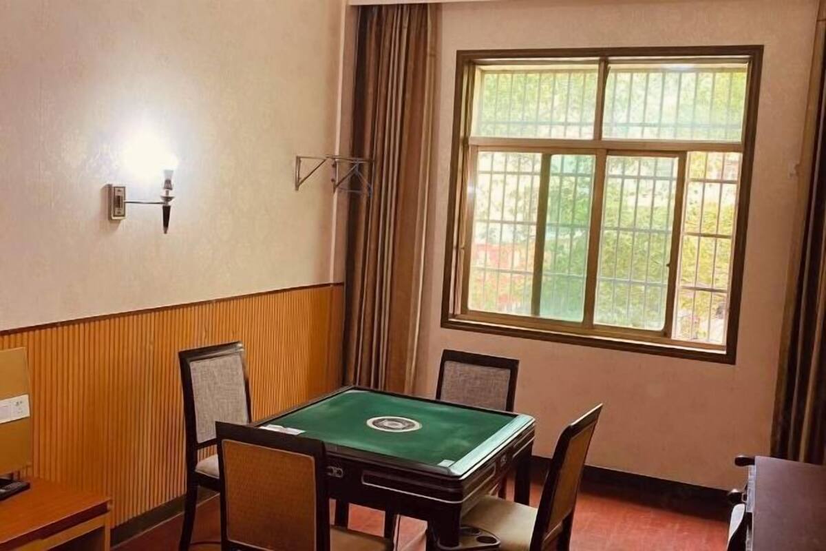Una habitación con mesa de billar verde, paneles de madera, un ventanal con barrotes y una lámpara fijada a la pared.