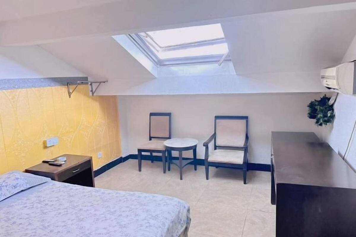 Un dormitorio con tragaluces, una cama, un escritorio y dos sillas.